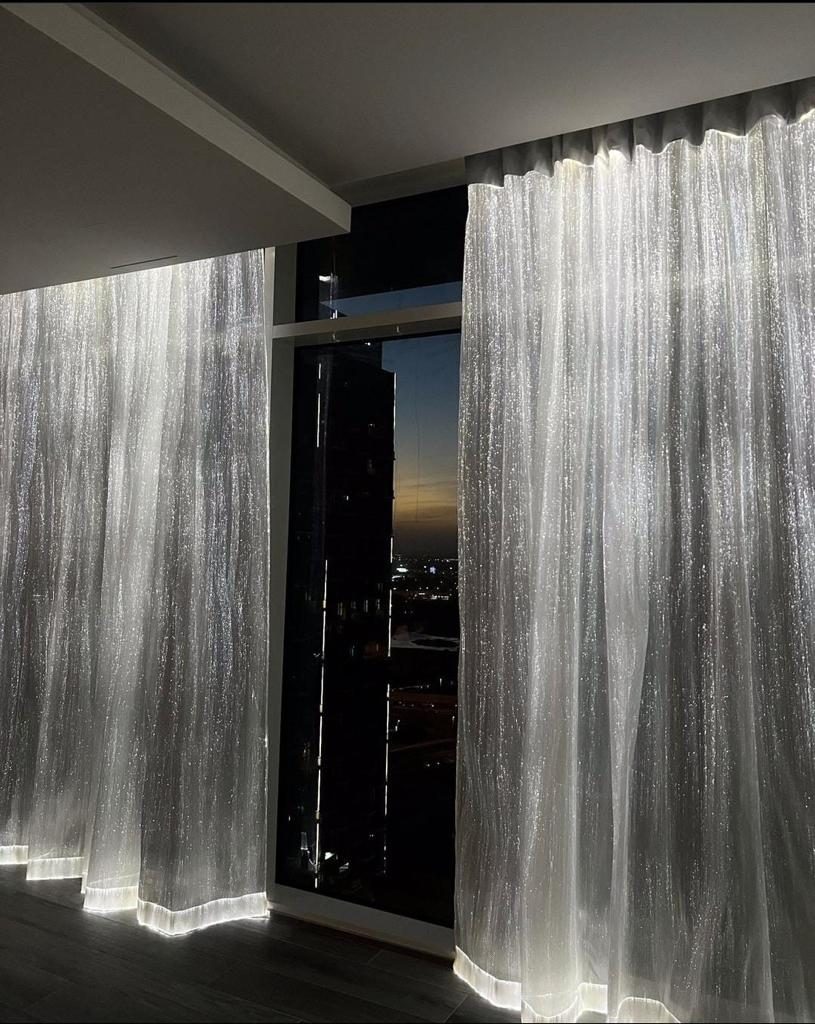 Illuminated sheer curtains against a city skyline at dusk